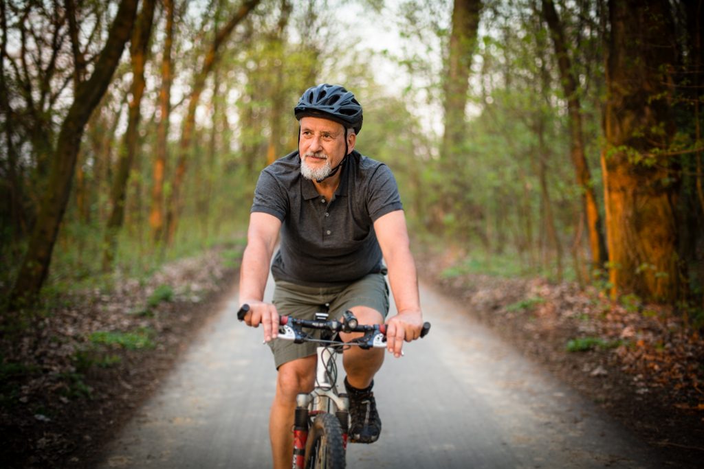 An older man riding a bike along a woodland track