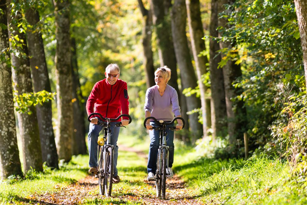 AN elderly couple riding bicycles together in the woods